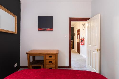 a bedroom with a red bed and a wooden table at Bazpackers in Inverness