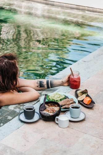 a woman laying next to a pool with a table of food at Flowers & Fire Yoga Garden in Gili Air