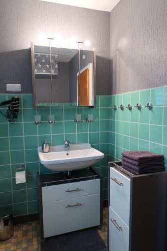 a bathroom with a sink and a mirror and green tiles at Ferienwohnung Wildung in Lüneburg