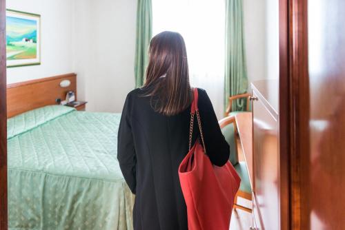 a woman standing in a bedroom with a red bag at Point Hotel in Piove di Sacco