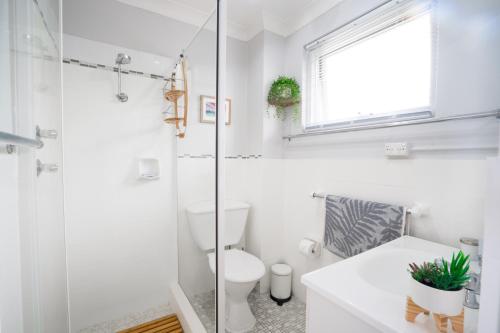 La salle de bains blanche est pourvue de toilettes et d'une douche en verre. dans l'établissement Sea Breeze Studio, à Kiama