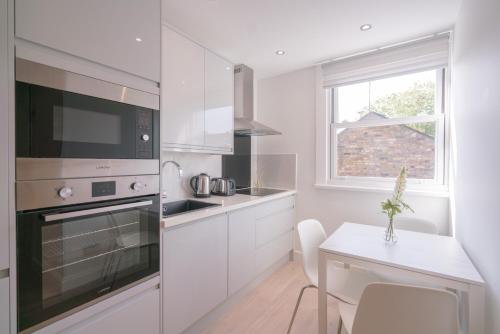 une cuisine avec des placards blancs, une table et une fenêtre dans l'établissement Cozy 2 Bed Room Tufnell Park Haven, à Londres