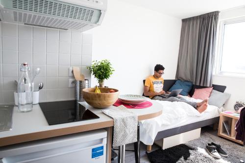 un hombre sentado en una cama en una pequeña cocina en Résidence Kley Toulouse en Toulouse