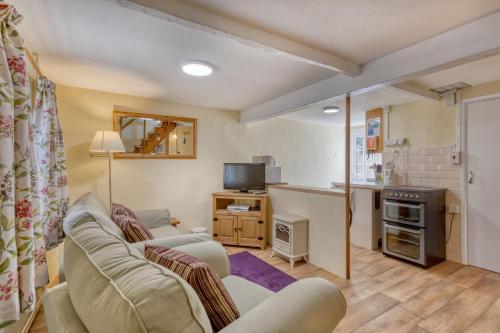 ein Wohnzimmer mit einem Sofa und einem TV sowie eine Küche in der Unterkunft La Bellieuse Cottages in St Martin Guernsey