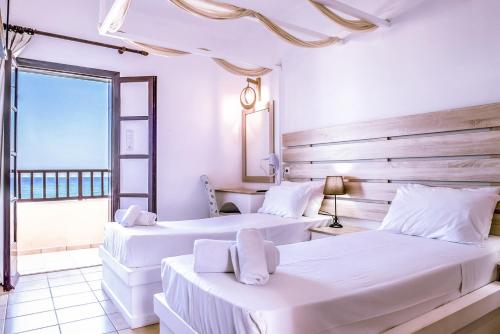 2 Betten in einem weißen Zimmer mit Fenster in der Unterkunft Porto Greco Village Beach Hotel in Hersonissos