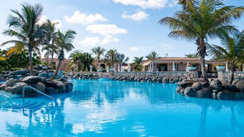 a pool at a resort with blue water and palm trees at Palm Oasis Maspalomas in Maspalomas