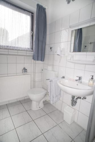 a white bathroom with a toilet and a sink at Hotel Garni Haus Schönberger in Heiligenhaus
