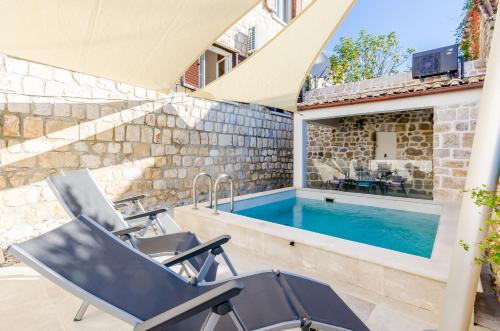 a swimming pool with two chairs next to a house at Apartments Villa Agava in Cavtat