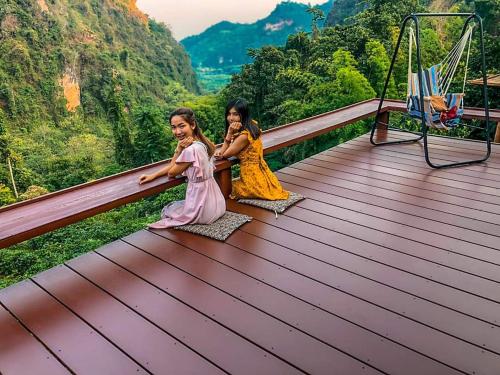 two little girls sitting on a wooden deck with mountains in the background at ม่านฟ้า โฮมสเตย์ MaanFah Homestay in Chiang Rai