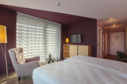 a bedroom with a bed and a chair and a window at Links Leuk Golfresort in Susten
