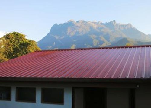 a building with a red roof with a mountain in the background at Mile 36 Lodge in Kundasang