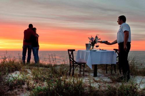 a man standing at a table on the beach at sunset at Apartamenty Mesa Grill Restaurant Cafe in Dźwirzyno