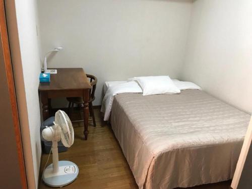 ein kleines Schlafzimmer mit einem Bett und einem Schreibtisch mit einem Ventilator in der Unterkunft Weekly Harbourview Mansion Main Building / Vacation STAY 76120 in Naha