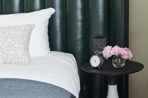 a bed with a table with a clock and flowers at Fitler Club in Philadelphia
