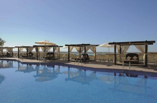 a swimming pool with chairs and umbrellas next to it at Radisson Blu Hotel, Abu Dhabi Yas Island in Abu Dhabi