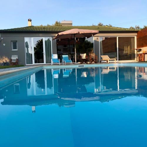 a swimming pool with an umbrella and a house at Sunlit Pool House in Posidhonía