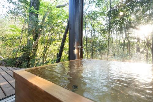 a hot tub in front of a window with trees at Sen-no-Mori in Aso