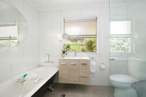 a white bathroom with a tub and a toilet and a sink at Camellia Cottage in Wentworth Falls