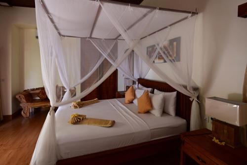 Bahari Villa Tejakula في تيجاكولا: غرفة نوم مع سرير مظلة مع ملاءات ووسائد بيضاء