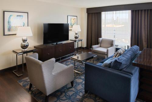 a living room with a couch and chairs and a television at The Arch Convention Hotel in Saint Louis