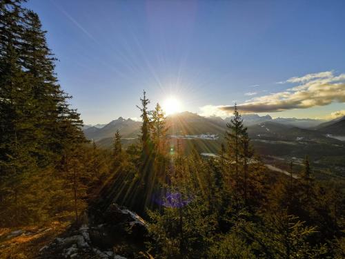a sun setting over a mountain with trees in the foreground at Gästehaus Simon in Krün