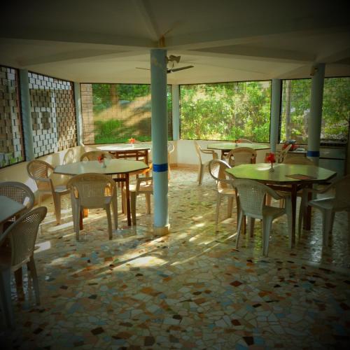 an empty restaurant with tables and chairs and windows at New Creation Guest House in Auroville