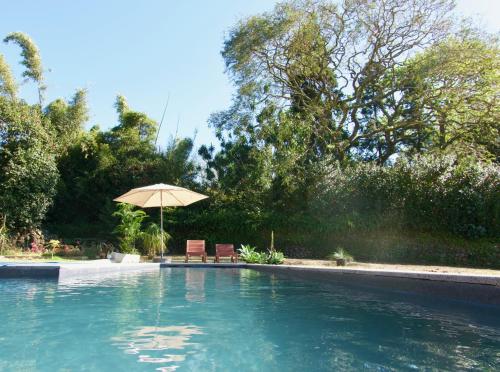 a swimming pool with an umbrella and two chairs at #Areias Houses 9 in Furnas