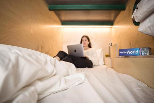 a woman sitting on a bed using a laptop at Green Marmot Capsule Hotel Zürich in Zürich