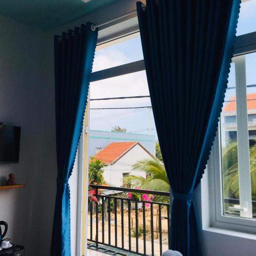 a window with blue curtains looking out at a balcony at An Bang Sea Adventure Homestay Hoi An in Hoi An