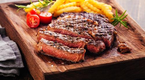 a wooden cutting board with steak and french fries at Hotel Garden Club in Braşov