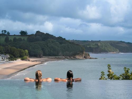 dos personas sentadas en el agua mirando a una playa en St Brides Spa Hotel & Village Apartments en Saundersfoot