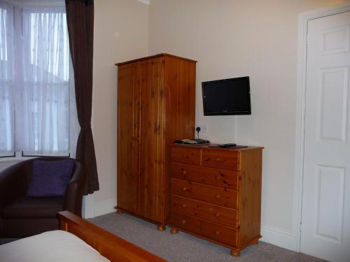 a bedroom with a wooden dresser with a television on it at Cornubia Guest House in Weymouth