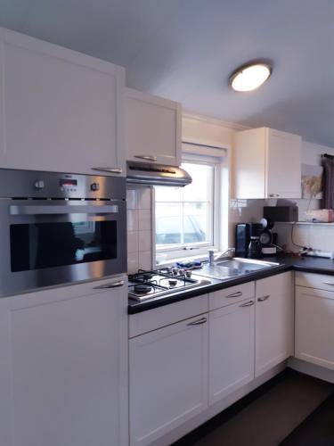 uma cozinha com armários brancos e um forno com placa de fogão em Zeepark Haerendyke em De Haan