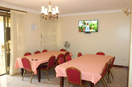 a dining room with two tables and chairs and a tv at Apricot Guest House Annex in Muyenga 