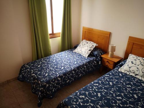 a bedroom with two beds and a window with green curtains at La Casita de Ana in San Sebastián de la Gomera