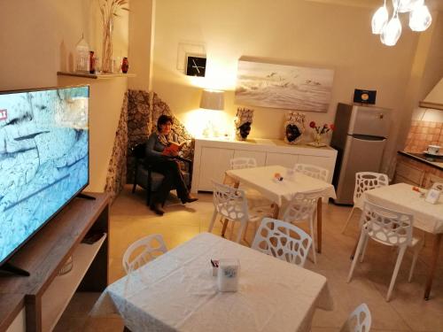a woman sitting in a chair in a kitchen with a flat screen tv at B&B Il Volo in Giardini Naxos