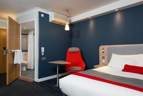 ミルトン・キーンズにあるホリデイイン エクスプレス ミルトンケインズのベッドと赤い椅子が備わるホテルルームです。