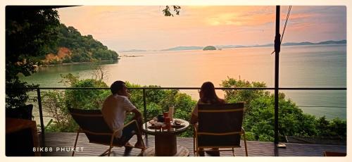 two people sitting at a table on a balcony overlooking the water at 8IK88 Resort, Phuket - SHA Extra Plus in Por Bay