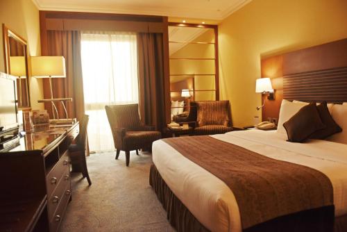 a hotel room with a bed and a desk and chair at Golden Tulip Bahrain in Manama