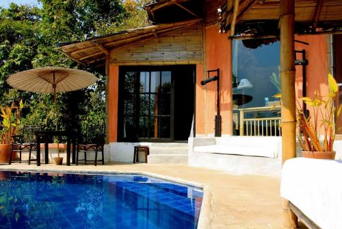 a swimming pool with an umbrella next to a house at Phu Chaisai Chiang Rai Mountain Resort in Mae Salong Nai