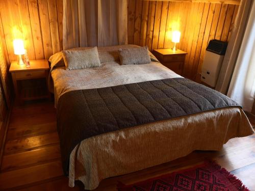 Un dormitorio con una cama con dos lámparas sobre dos mesas. en Cabaa Oregn con hot tub exclusivo cerca de termas y lago, en Coñaripe