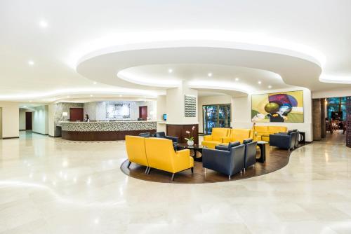 a lobby of a hospital with yellow chairs and tables at Holiday Inn Convention Center by IHG in Managua