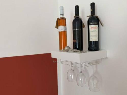 three wine bottles and wine glasses on a shelf at Talìa in Agira