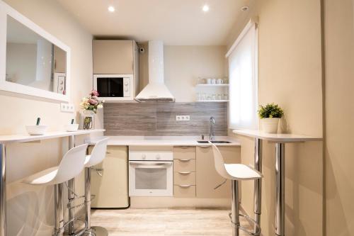 a kitchen with white counters and white chairs at Chic Gran Via Apartment in Barcelona