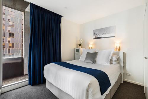 a bedroom with a large bed with blue curtains and a window at Central Melbourne CBD Apartment with Gym and Pool in Melbourne