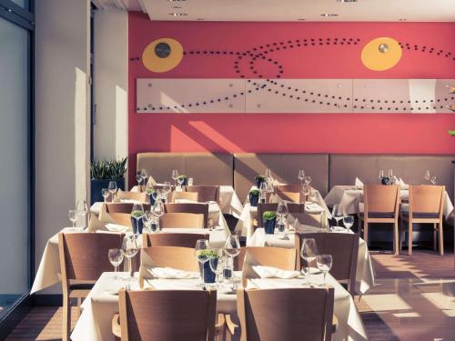 a restaurant with white tables and chairs and a red wall at Mercure Hotel Mannheim am Friedensplatz in Mannheim