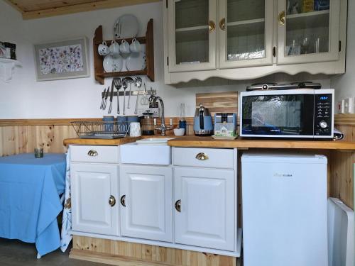 eine Küche mit weißen Schränken und einer Mikrowelle in der Unterkunft The Old Mill Shepherds Hut in Okehampton