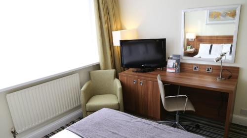 a hotel room with a desk with a television and a chair at Holiday Inn Runcorn M56 Junction 12 by IHG in Runcorn