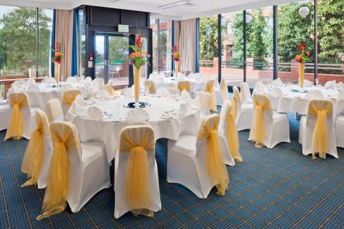 a banquet hall with white tables and chairs with yellow bows at Holiday Inn Runcorn M56 Junction 12 by IHG in Runcorn