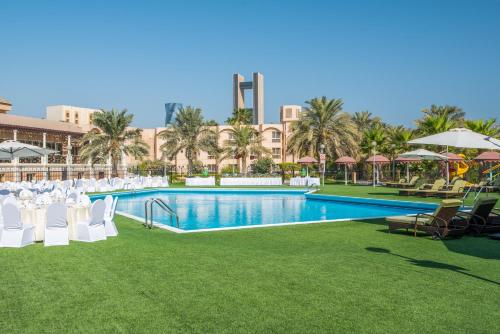 a resort pool with white chairs and umbrellas at Crowne Plaza Bahrain, an IHG Hotel in Manama